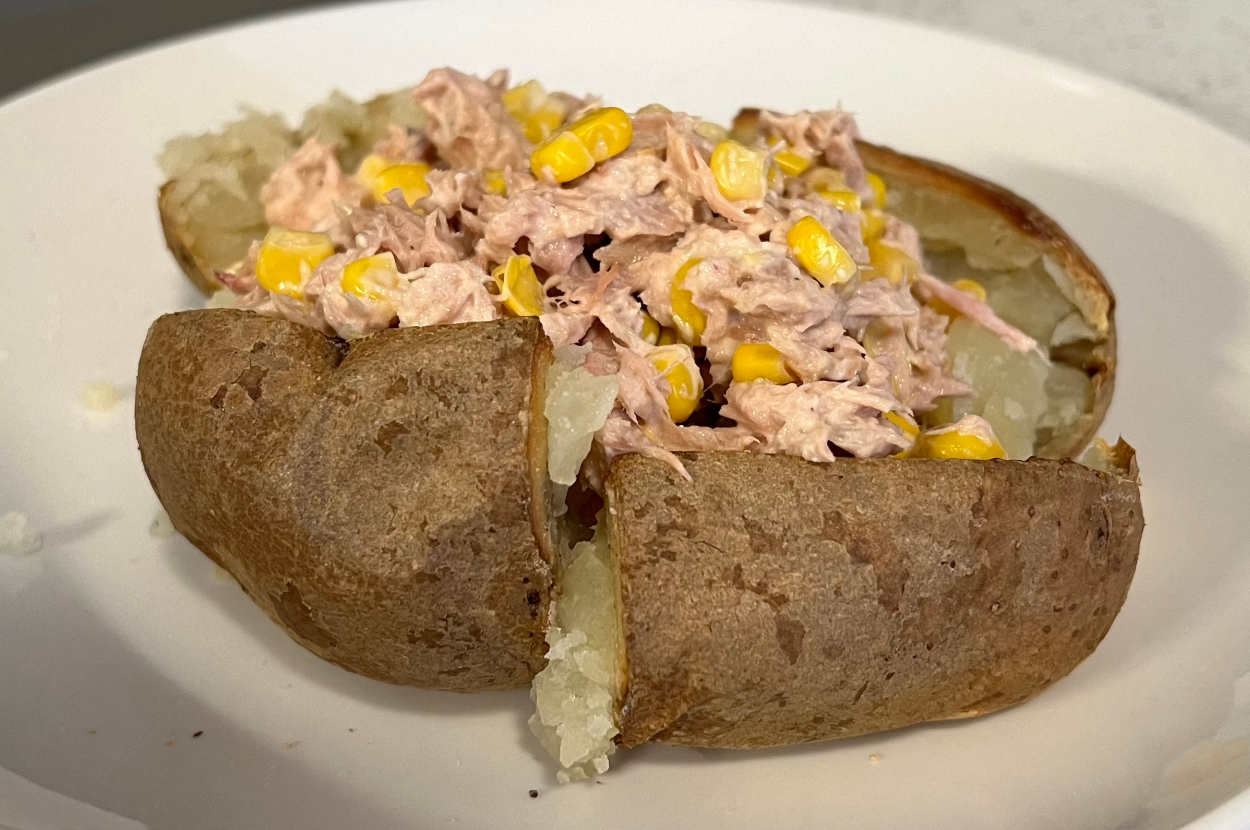 Baked potato topped with a mixture of tuna and corn on a plate