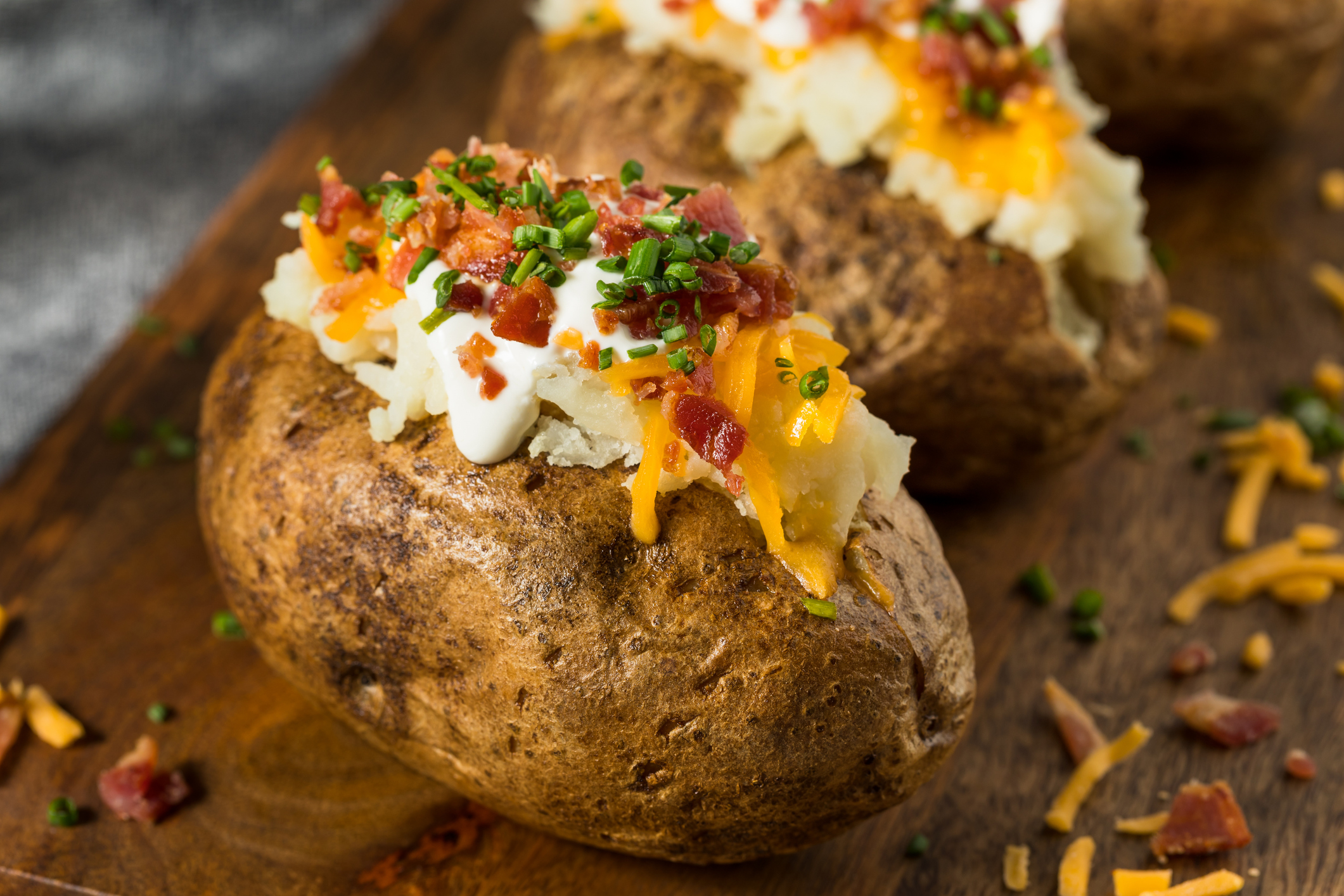 Loaded baked potatoes topped with sour cream, shredded cheese, bacon bits, and chopped chives on a wooden surface