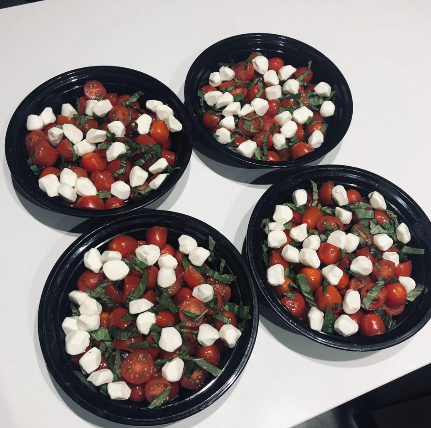 Four black bowls each filled with cherry tomatoes, fresh basil, and small mozzarella balls resembling a caprese salad