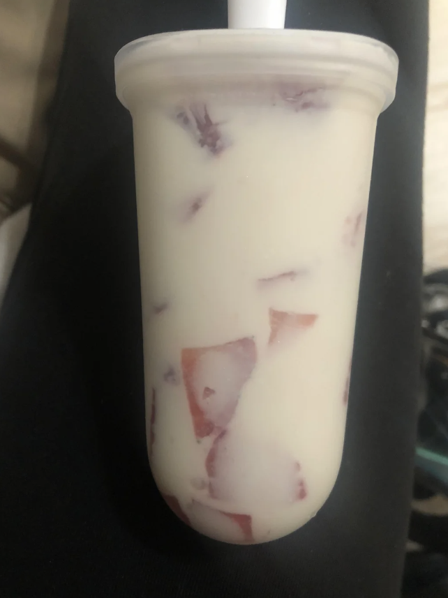 A yogurt popsicle with visible chunks of strawberries inside, held by a person in their hand